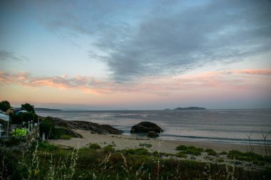 İspanya, Galiçya 'da yaz tatilinde kayaların ve deniz fenerinin fotoğrafı. Mavi okyanus, boş sahil.