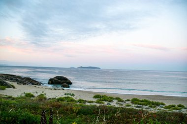 İspanya, Galiçya 'da yaz tatilinde kayaların ve deniz fenerinin fotoğrafı. Mavi okyanus, boş sahil.