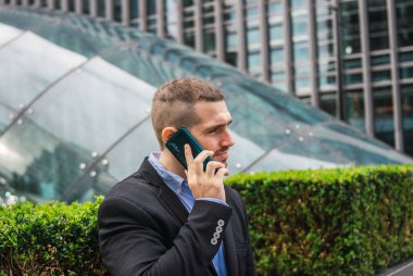 Genç ve çekici bir iş adamının bir görüşme ayarlamak için telefonda konuştuğu fotoğraf. Şık günlük giysiler giyiyor. 