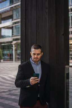 Telefonunu kontrol eden genç ve çekici bir iş adamının fotoğrafı. Havalı kıyafetler giyiyorlar. Girişimci stili