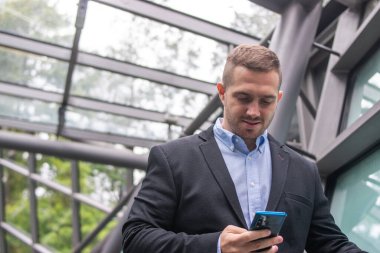 Genç ve çekici bir iş adamının resmi. Sıradan kıyafetler giyip toplantıdan önce telefonunu kontrol ediyor..