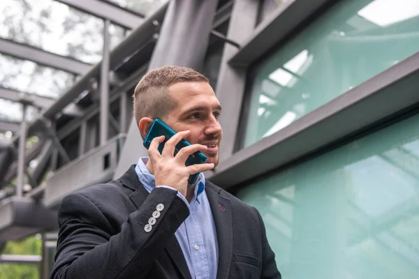 Photo of a young and attractive business man talking on the phone to fix a meeting. Wearing smart casual clothes