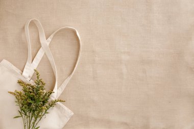 Boş bej renkli keten keten çanta ve keten kumaş üzerinde sarı çiçekler. Çevre dostu stil. Çevre koruma geri dönüşüm kavramı.