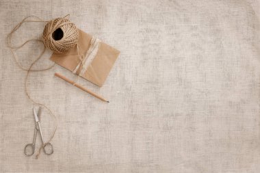 Top view moda tasarımcısı arkaplan konsepti. Düz yatar koli defteri aksesuarları. Makas, ev stüdyosundaki kahverengi keten kumaşın üzerindeki sicim. Tasarım modeli için alan