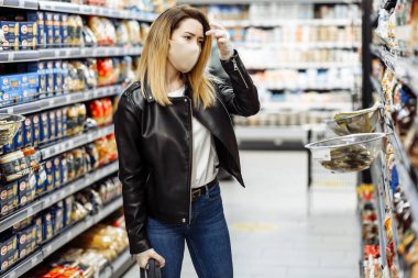 Shopping during the coronavirus Covid-19 pandemic. A young woman buys food in a supermarket with shopping cart. Woman in facial mask and gloves to prevent infection. clipart