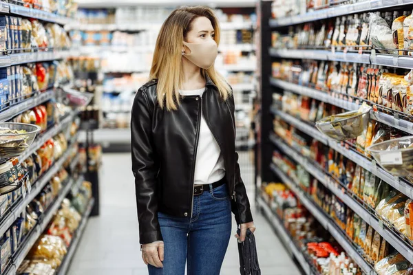 Markette maske takan ve lastik eldiven takan güzel bir genç kadın. Coronavirüs krizi sırasında ya da covid19 salgını sırasında raftan alışveriş malzemesi almak isteyen bir kız..