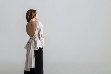 Beyaz açık arka gömlekli ve siyah pantolonlu güzel, çekici bir model. Gri arka planda, telif alanı ile izole edilmiş. Minimalist moda görünüşü
