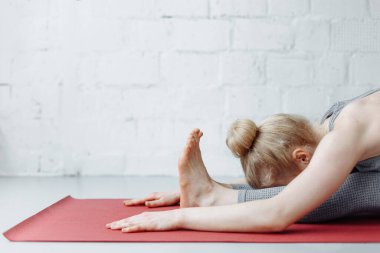 Triang mukhaikapada pashchimottanasana yoga pozisyonunda bir kadın. Genç ve çekici bir kadın yoga yapıyor, spor kıyafetleri giyiyor, pantolon giyiyor ve üstte, kapalı alanda, yoga stüdyosunda.