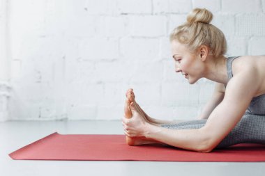 Triang mukhaikapada pashchimottanasana yoga pozisyonunda bir kadın. Genç ve çekici bir kadın yoga yapıyor, spor kıyafetleri giyiyor, pantolon giyiyor ve üstte, kapalı alanda, yoga stüdyosunda.