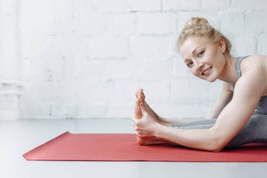 Triang mukhaikapada pashchimottanasana yoga pozisyonunda bir kadın. Genç ve çekici bir kadın yoga yapıyor, spor kıyafetleri giyiyor, pantolon giyiyor ve üstte, kapalı alanda, yoga stüdyosunda.