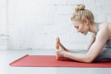 Triang mukhaikapada pashchimottanasana yoga pozisyonunda bir kadın. Genç ve çekici bir kadın yoga yapıyor, spor kıyafetleri giyiyor, pantolon giyiyor ve üstte, kapalı alanda, yoga stüdyosunda.