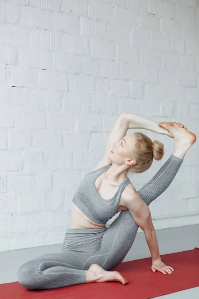 Yoga yapan esnek kadın gri arka planda Parivritta Kraunchasana 'ya poz veriyor. Genç ve çekici bir kız yoga yapıyor, spor kıyafetleri giyiyor, pantolon ve bluz giyiyor, kapalı alanda, yoga stüdyosunda.