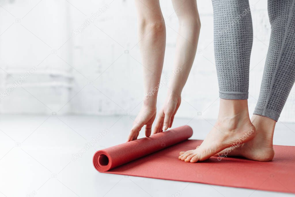 Young yoga Woman rolling her pink mat after a yoga class on wooden floor near a window, close up