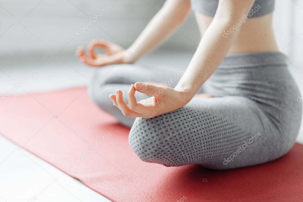 Meditation concept. Close up of hands of young office yogi woman sitting cross legged in yoga Easy Sukhasana Pose on pink mat, meditating with fingers in Jnana mudra