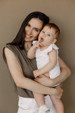 Açık renk elbiseli bir kadın, küçük tatlı bir kızla eğleniyor. Anne, küçük kız pastel bej duvar arkasında izole edilmiş, stüdyo portresi. Anneler Günü aşk ailesi, ebeveynlik çocukluk kavramı