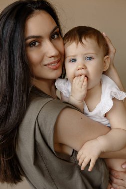 Açık renk elbiseli bir kadın, küçük tatlı bir kızla eğleniyor. Anne, küçük kız pastel bej duvar arkasında izole edilmiş, stüdyo portresi. Anneler Günü aşk ailesi, ebeveynlik çocukluk kavramı