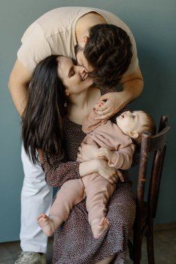 Pembe elbiseli, yeni doğmuş bir bebeği kucağında tutan genç adam ve kadının portresi. Beyaz tenli, gülümseyen anne ve baba şefkatle kucaklayan yeni doğan sevimli çocuk. Mutlu aile kavramı