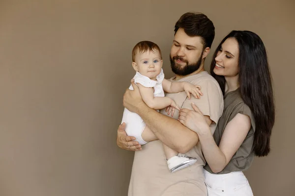 Pembe elbiseli, yeni doğmuş bir bebeği kucağında tutan genç adam ve kadının portresi. Beyaz tenli, gülümseyen anne ve baba şefkatle kucaklayan yeni doğan sevimli çocuk. Mutlu aile kavramı