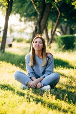 Parktaki çimlerde oturan sıradan tarzda bir kız.
