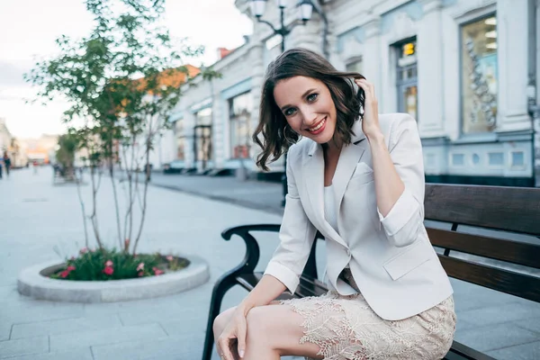 Beyaz takım elbiseli bir kız sokakta bir bankta oturuyor.