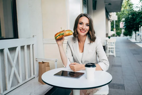 Beyaz ceketli bir kız bir kafede kahve, sandviç ve grafik tabletle oturuyor.