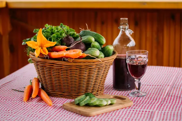 Masada bir sepet sebze, bir şişe şarap ve bir bardak var.