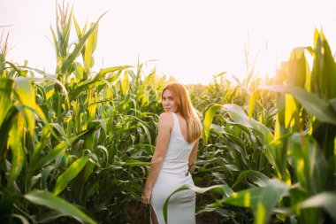 Kızıl saçlı kız mısır tarlasında gülümsüyor.