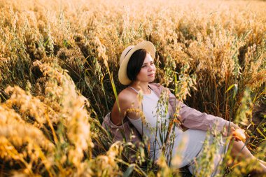 Hasır şapkalı bir kız tarlada oturuyor.