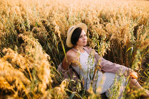 Hasır şapkalı bir kız tarlada oturuyor.