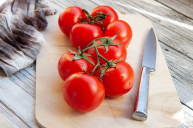 Kırmızıdomatesler dallarda, kesme tahtasında, açık ahşap arka planda.