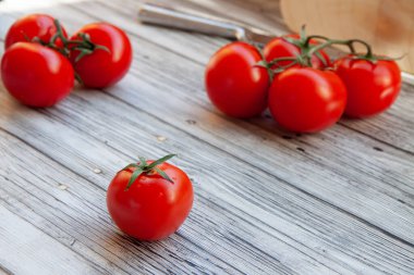 Kırmızıdomatesler dallarda, kesme tahtasında, açık ahşap arka planda.