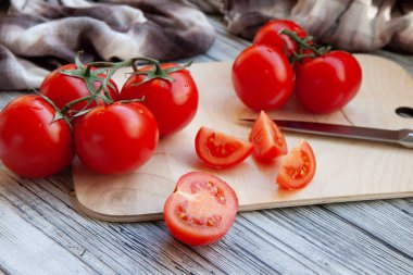 Kırmızıdomatesler dallarda, kesme tahtasında, açık ahşap arka planda.