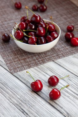 Beyaz fincanda kiraz çileği, açık mutfak peçetesi, açık ahşap arka plan.