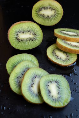 Kesilmiş ve tüm kivi meyvesi koyu bir arka plana karşı, dikey düzenleme