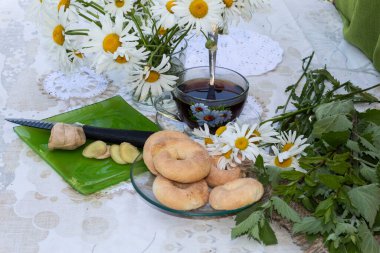 Bir fincan çayın yanında papatya çayı, limon merhemi ve nane otu var. Tabakta kurabiyeler var. Yeşil tabakta zencefil kökü var, dilimlenmiş.