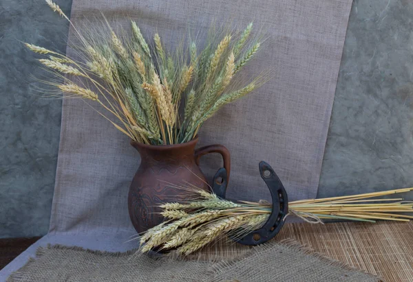 On the table is a jug with ears of wheat and a horseshoe in which ears of wheat are threaded.