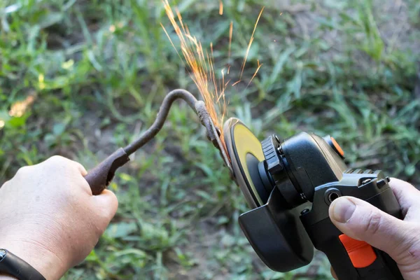 A man grinds a garden tool with a grinder.