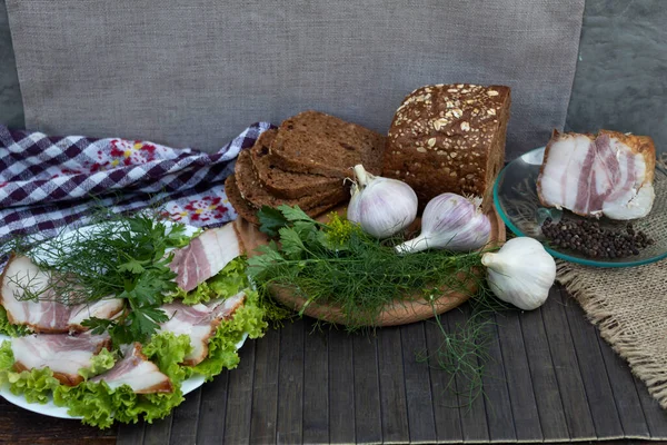 Marul yapraklarının üzerinde pastırma, dereotu ve maydanoz parçaları var. Yakınlarda doğranmış siyah ekmek, sarımsak, domuz pastırması ve biber var.