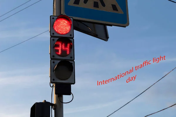 A red traffic light is on against a blue sky. The stopwatch shows the number of seconds until the signal changes. On the side there is an inscription: 