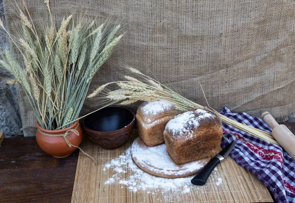 Masanın üzerinde iki somun ekmek, un, bir bıçak, bir kase toprak ve buğday var..