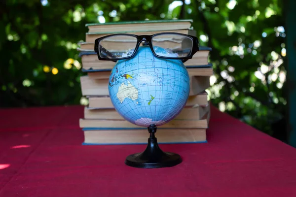 A school globe with toy eyes and glasses stands on a red tablecloth against the backdrop of a stack of books