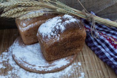 Masanın üzerinde, yuvarlak bir kesim tahtasının üzerinde iki somun ekmek, buğday ve un var.