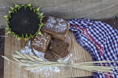 Masanın üzerinde üç somun ekmek, buğday, un ve olgun siyah taneli bir ayçiçeği var..