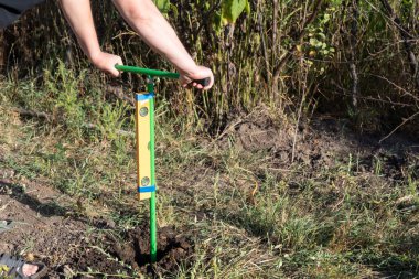 Elinde bir el matkabı olan bir adam, bina seviyesinin belirlendiği, bahçeye bir delik açar..
