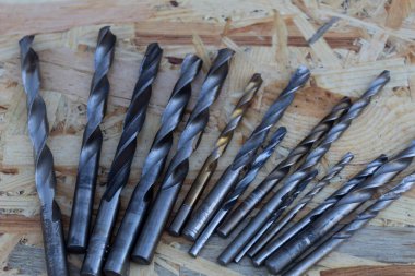 Farklı çaplarda metal matkaplar ahşap bir zeminde yatar..