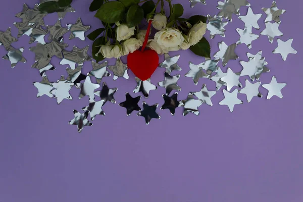 Metal stars are scattered on a purple background, white roses and a red heart lie.