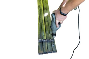 İzole et. Bir adam elektrikli matkapla metal borularda delik açıyor.