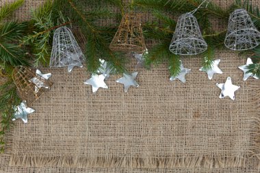 Ladin dalları ve beş yeni yıl çanı jüt kumaşın üzerinde yatıyor. Yakınlarda yıldızlar şeklinde konfeti uzanır..