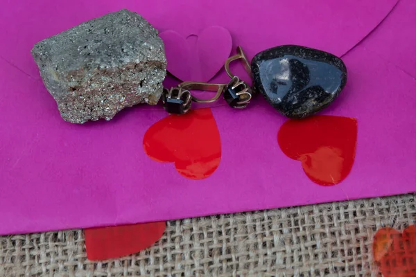 On the pink envelope are earrings with a black stone and two natural semi-precious stones - black onyx and arsenopyrite.