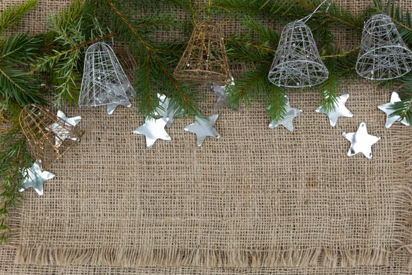 Ladin dalları ve beş yeni yıl çanı jüt kumaşın üzerinde yatıyor. Yakınlarda yıldızlar şeklinde konfeti uzanır..